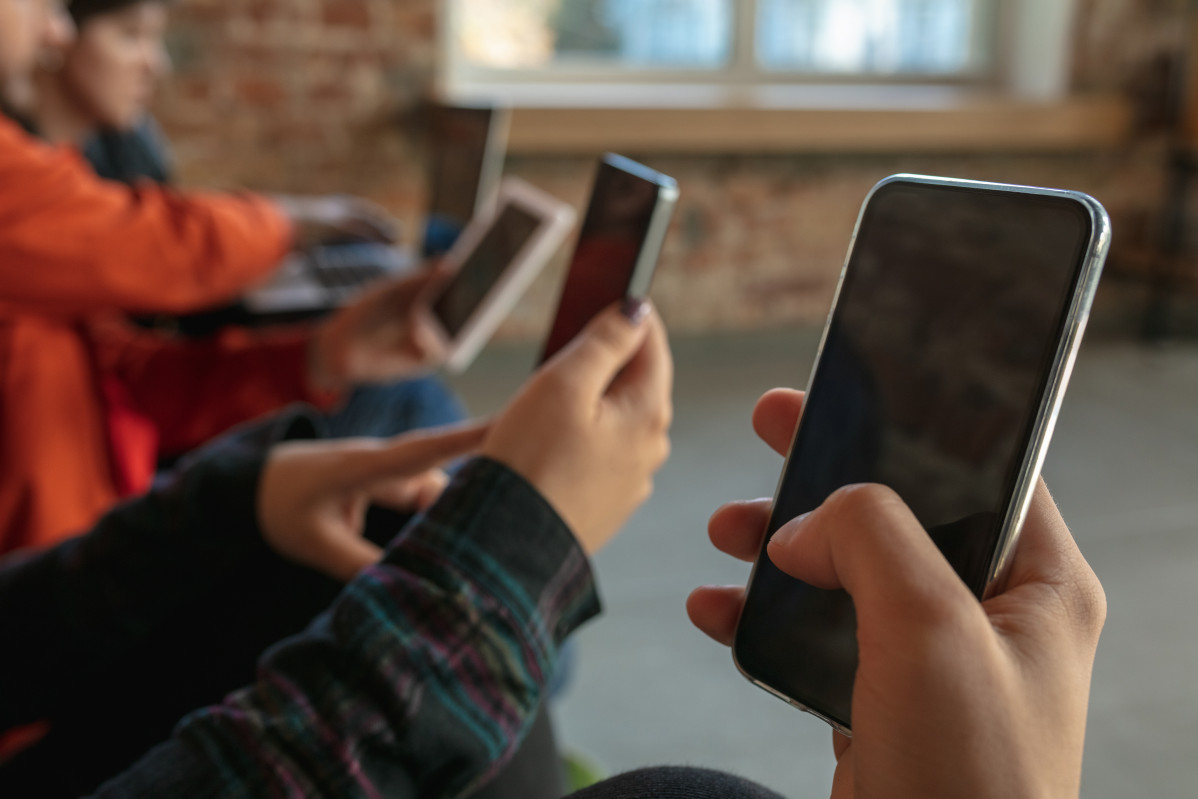 Group of happy young young people sitting on sofa together sharing news photos or videos from smartphones reading articles or playing games and having fun social media modern technologies